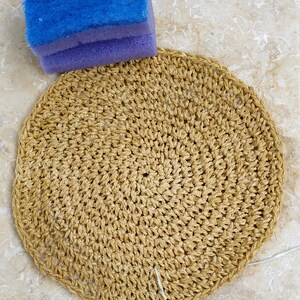 May include: A round, crocheted, beige-colored placemat with a white string attached to the bottom.