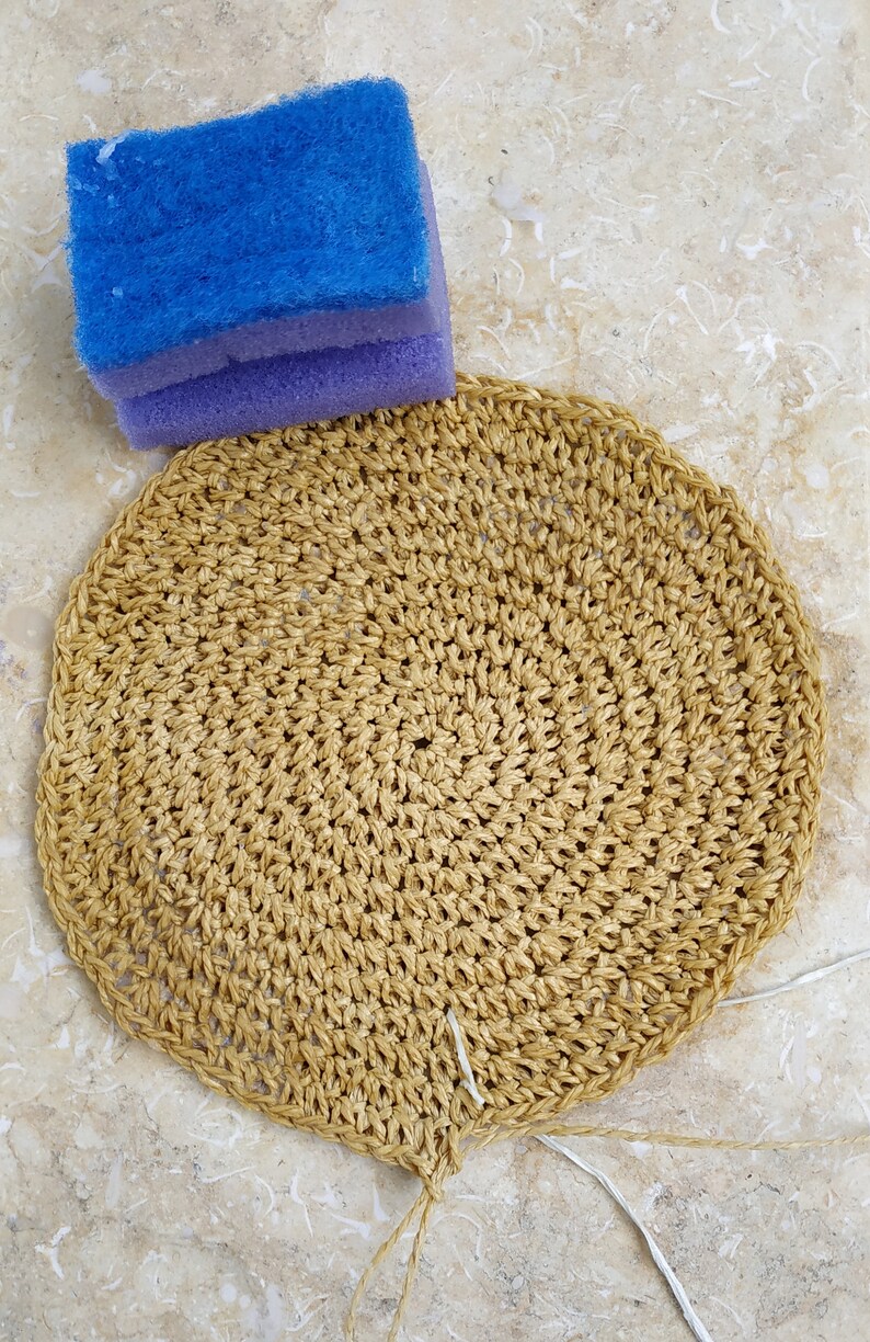 May include: A round, crocheted, beige-colored placemat with a white string attached to the bottom.