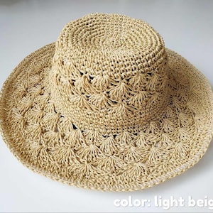 Op de afbeelding: Lichtbeige zonnehoed met brede rand. De hoed is gemaakt van geweven stro en heeft een decoratief opengewerkt patroon op de rand en de kroon. De hoed is lichtbeige van kleur en is ontworpen voor bescherming tegen de zon.