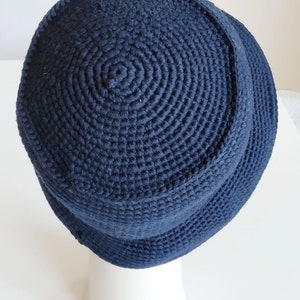 May include: A dark blue crocheted bucket hat. The hat is made with a thick yarn and has a simple, classic design.