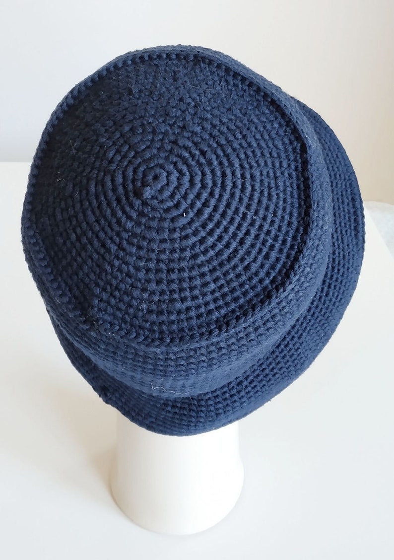 May include: A dark blue crocheted bucket hat. The hat is made with a thick yarn and has a simple, classic design.