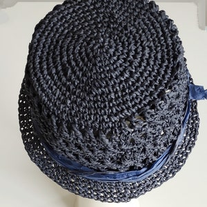 May include: A dark blue crocheted hat with a wide brim and a navy blue ribbon around the crown.