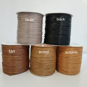Pu&ograve; includere: Cinque bobine di nastro di rafia piatto disposte su due file. La fila superiore presenta bobine color tortora e nero. La fila inferiore contiene bobine color tan, legno e autunno. Ogni bobina &egrave; etichettata con il nome del colore in bianco.