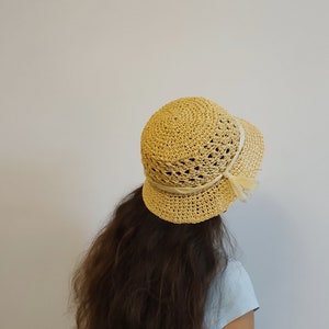 May include: A light yellow crocheted sun hat with a wide brim and a white ribbon.