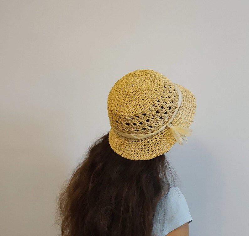 May include: A light yellow crocheted sun hat with a wide brim and a white ribbon.