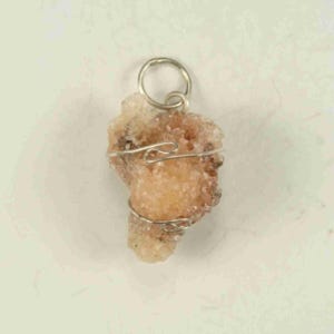 May include: A natural, irregularly shaped pendant with a light peach hue, wrapped in silver-colored wire. The pendant has a small, circular loop at the top for hanging. The stone has a rough, textured surface.