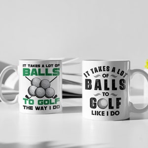 May include: Two white ceramic mugs with black and green text. One mug says "IT TAKES A LOT OF BALLS TO GOLF THE WAY I DO" with golf balls and clubs. The other says "IT TAKES A LOT OF BALLS TO GOLF LIKE I DO" with a golf ball.