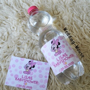 以下が含まれることがあります： ピンクのキャップが付いた透明なプラスチック製のウォーターボトル。ミニーマウスのラベルが付いています。ラベルにはピンク色の文字で「LISAS BABYSOWER」と「20.02.2020」と書かれています。ボトルの横にはお揃いのカードがあります。