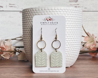 Puede incluir: Un par de pendientes geométricos con estampado verde claro y blanco con aros dorados. Los pendientes están en una tarjeta blanca con el texto "SIMPLY GRACE by Dakota Country Designs" y la dirección del sitio web "dakotacountrydesigns.etsy.com".