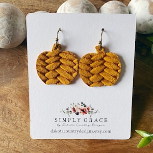 May include: A pair of mustard yellow pumpkin-shaped earrings with a woven texture. The earrings are on a white card with the text "SIMPLY GRACE by Dakota Country Designs dakotacountrydesigns.etsy.com"
