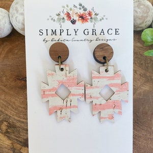 May include: A pair of pink and white geometric patterned earrings with cork and wood accents. The earrings are on a white card with the text "SIMPLY GRACE by Dakota Country Designs" and the website "dakotacountrydesigns.etsy.com".