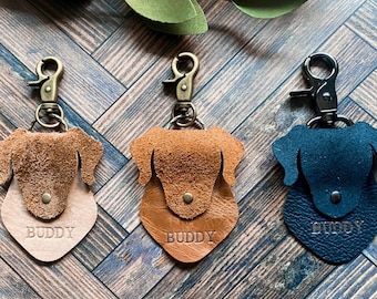 May include: Three leather dog head keychains with metal rings and clips. The keychains are brown, tan, and black. Each keychain has the word "BUDDY" engraved on the front.