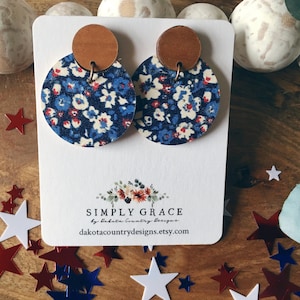 May include: A pair of blue and white floral patterned earrings with brown wooden accents. The earrings are displayed on a white card with the text "SIMPLY GRACE by Dakota Country Designs dakotacountrydesigns.etsy.com".