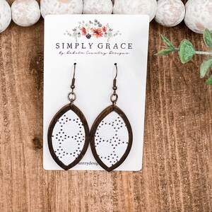 May include: White leather earrings with a brown wood frame and a dotted pattern. The earrings are on a white card with the text "SIMPLY GRACE by Lakota Country Designs".