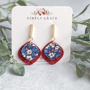 May include: A pair of red and blue floral dangle earrings with gold accents. The earrings are on a white card with the text "SIMPLY GRACE".
