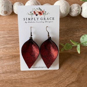 Op de afbeelding: Een paar rode leren oorbellen met een metallic afwerking. De oorbellen zijn traanvormig en hebben een eenvoudige haaksluiting. De oorbellen worden gepresenteerd op een witte kaart met de tekst "SIMPLY GRACE by Dakota Country Designs".