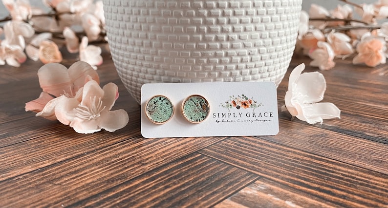 Peut inclure: Une paire de boucles d'oreilles clous dor&eacute;es avec un motif marbr&eacute; vert et brun. Les boucles d'oreilles sont pr&eacute;sent&eacute;es sur une carte blanche avec le texte "SIMPLY GRACE by Dakota Country Designs".