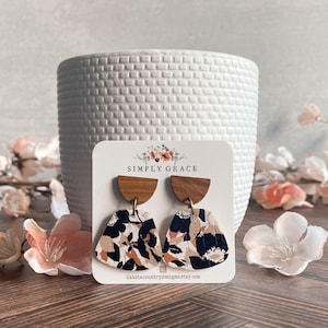 Puede incluir: Un par de pendientes con estampado floral y detalles de madera en forma de semicírculo. Los pendientes se muestran en una tarjeta blanca con el texto "SIMPLY GRACE" y "dakotacountrydesignatetsy.com".