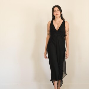 May include: A sleeveless black midi dress featuring a deep V-neckline with a central twist detail at the bodice. The dress is constructed from a lightweight, semi-sheer fabric that falls to a mid-calf length with a slightly asymmetrical hemline.