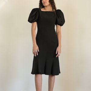 Puede incluir: Un vestido midi negro con mangas abullonadas y escote cuadrado. El vestido tiene un corpiño ajustado y una falda acampanada.