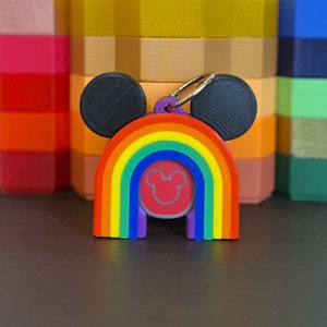 May include: A rainbow-colored keychain with Mickey Mouse ears and a Mickey Mouse head in the center. The keychain is made of plastic and has a silver ring.