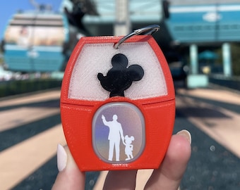 Könnte beinhalten: Roter Plastik-Schlüsselanhänger mit einer weißen Mickey-Maus-Silhouette und einem holografischen Bild von Mickey Mouse und einem Freund. Der Schlüsselanhänger ist an einem silbernen Ring befestigt.