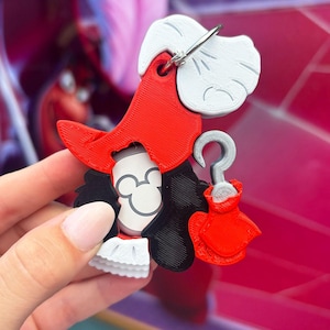 May include: A 3D-printed keychain featuring a cartoon character in red, white, black, and gray. The keychain depicts a character with a red hat, a white wig, and a black coat. A silver-colored metal ring is attached to the top.
