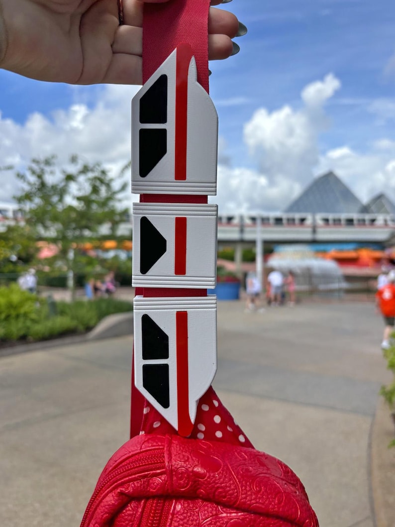 May include: A red and white monorail charm with black windows. The charm is attached to a red polka dot bag.