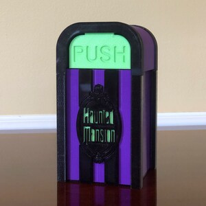 May include: A purple and black striped Haunted Mansion trash can with a green "PUSH" button on top.