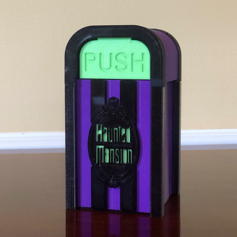 May include: A purple and black striped Haunted Mansion trash can with a green "PUSH" button on top.