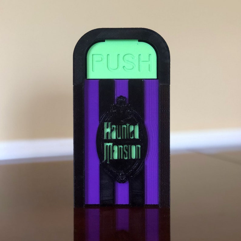 May include: A black and purple Haunted Mansion themed doorstop with a green "PUSH" button.