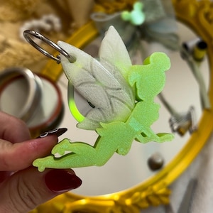 May include: A green glitter fairy keychain with a white glitter wing. The keychain has a silver ring attached to it.