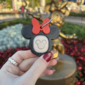 May include: A black and red 3D printed Minnie Mouse keychain with a white Mickey Mouse head on the front. The keychain has a silver clip.