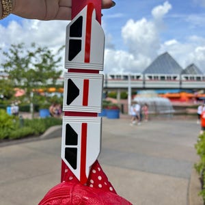 May include: A red and white monorail keychain with three cars attached to a red polka dot bag.