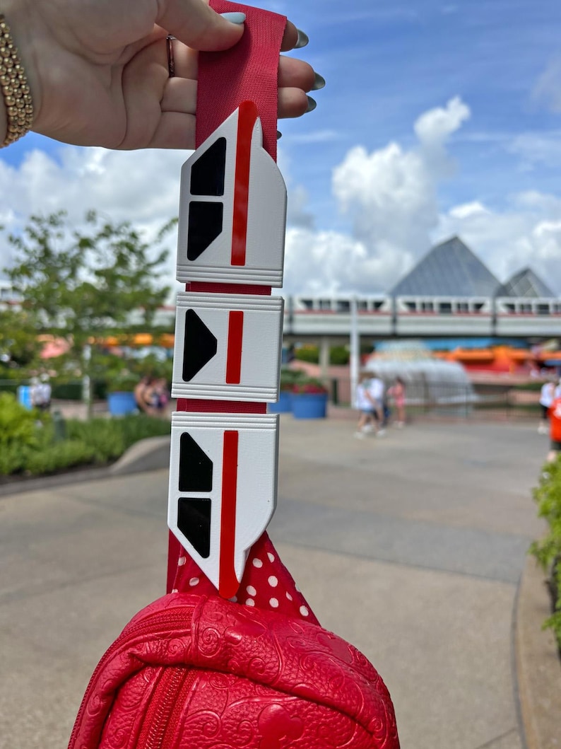 May include: A red and white monorail keychain with three cars attached to a red polka dot bag.