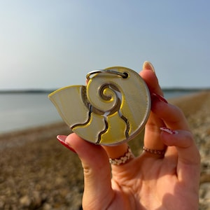 May include: A yellow and silver 3D printed seashell keychain. The seashell is a spiral shape with a textured surface.