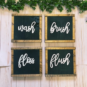 May include: Four wooden signs with black backgrounds and white lettering. The signs read "wash", "brush", "floss", and "flush".