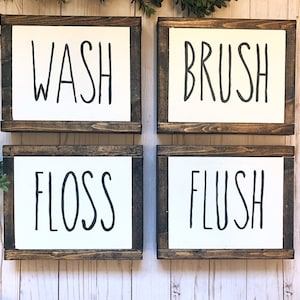 May include: Four wooden signs with white backgrounds and black text. The signs read "WASH", "BRUSH", "FLOSS", and "FLUSH".