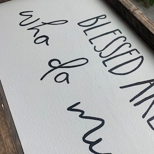 May include: A rectangular wooden sign with a white background and black cursive text that reads "Blessed and Whata Mess". The sign has a dark brown wooden frame.