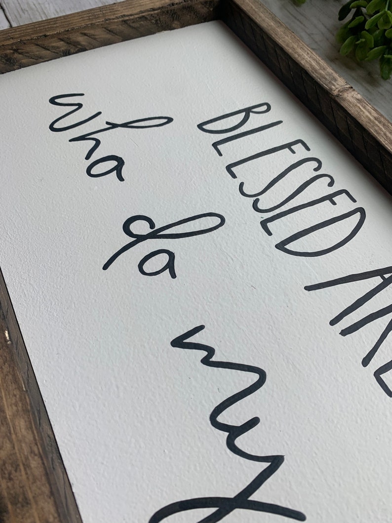 May include: A rectangular wooden sign with a white background and black cursive text that reads "Blessed and Whata Mess". The sign has a dark brown wooden frame.