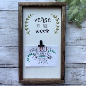 Könnte beinhalten: Ein Schild aus Holz mit dem Text "verse of the week" und einem Clip, der eine Karte mit dem Text "my cup runneth over" in schwarzer und grüner Schrift hält.