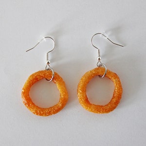 May include: A pair of dangle earrings featuring a fried onion ring design. The earrings are made of a gold-colored metal and have a silver hook.