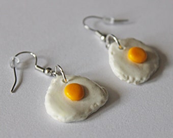 Puede incluir: Un par de pendientes de aro de plata con dijes de huevo frito blanco y amarillo.