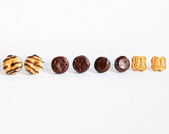 May include: A set of six miniature food earrings, including two chocolate-covered donuts, two chocolate chip cookies, and two square crackers.
