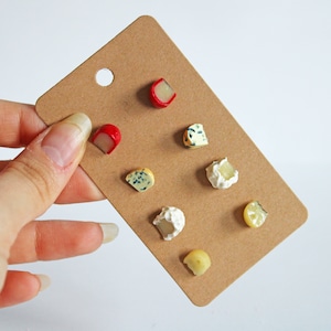 Könnte beinhalten: Eine braune Karte mit verschiedenen Miniatur-Käseformen, darunter rote, blaue und weiße Sorten. Die Käseformen sind in einem Raster auf der Karte angeordnet.