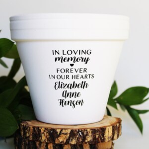 May include: White ceramic flower pot with the text "In loving memory" with a heart symbol, "Forever in our hearts", "Elizabeth Anne Henson".