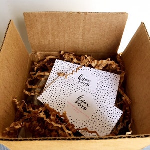 May include: A brown cardboard box with a white and black patterned card inside. The card has the text "Knox Pots" and "Custom Personalized Pots".