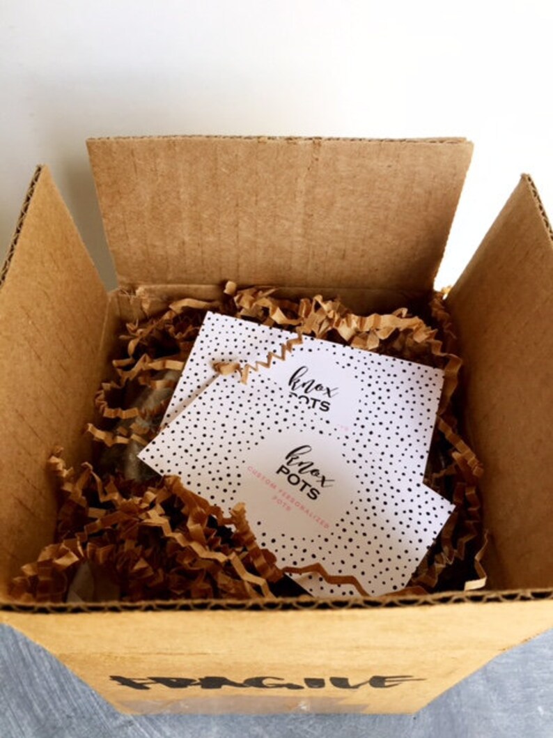 May include: A brown cardboard box with a white and black patterned card inside. The card has the text "Knox Pots" and "Custom Personalized Pots".