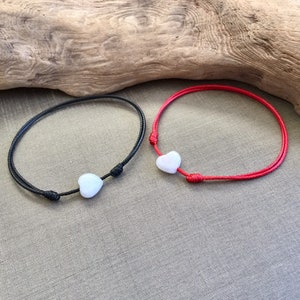 May include: Two friendship bracelets with white heart charms. One bracelet is black and the other is red.