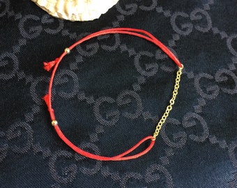May include: A red string bracelet with a gold chain accent and small gold beads.